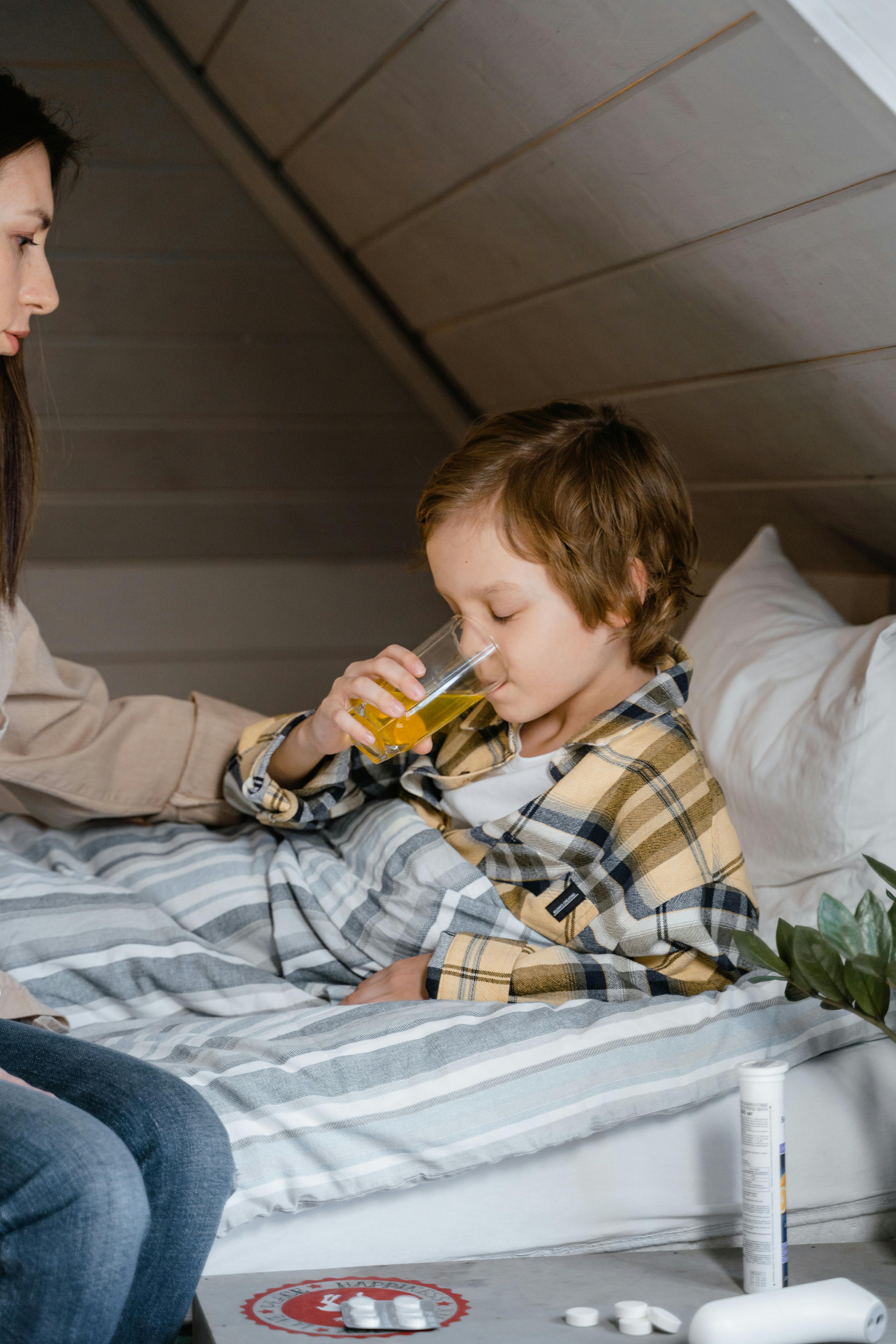 a kid lying on the bed while drinking from the clear glass