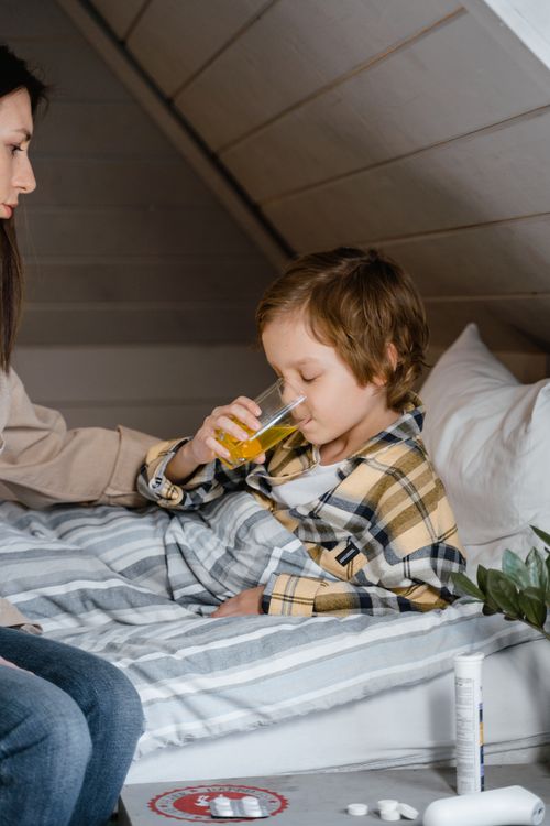 Free A young boy drinks juice while being comforted by his mother in a cozy bedroom setting. Stock Photo
