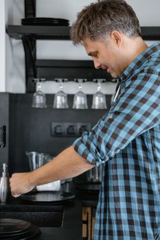 Side view of an adult man making coffee in a stylish kitchen.