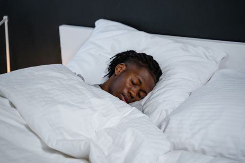 Free A young man resting peacefully in a bed with white sheets and a dark background. Stock Photo