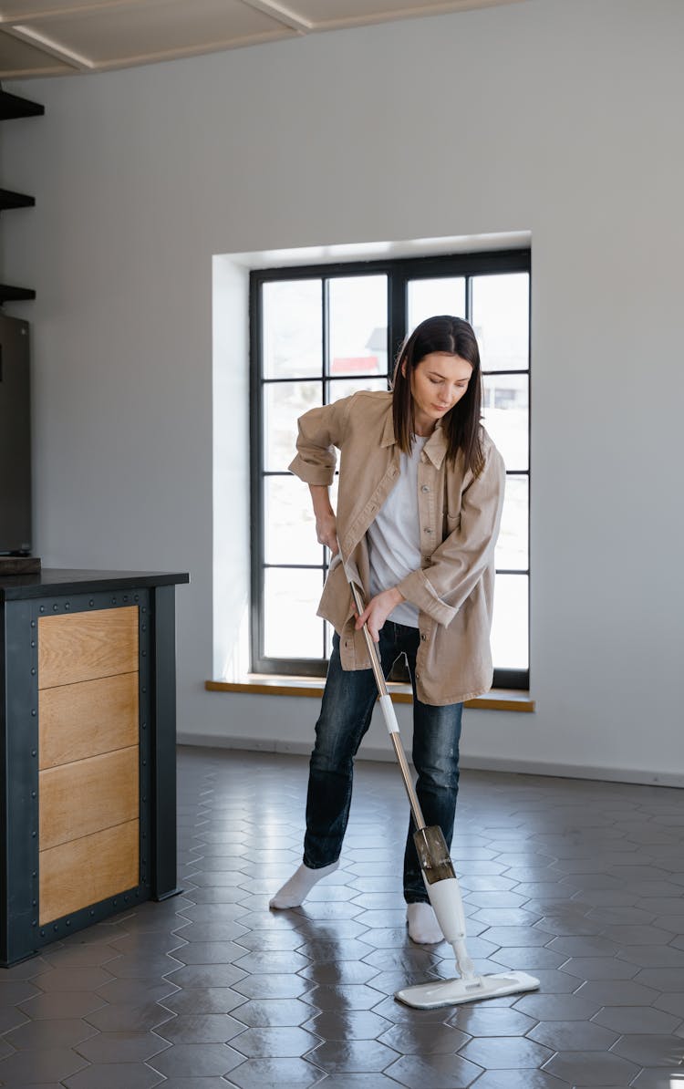 A Woman In Beige Coat Mopping The Floor