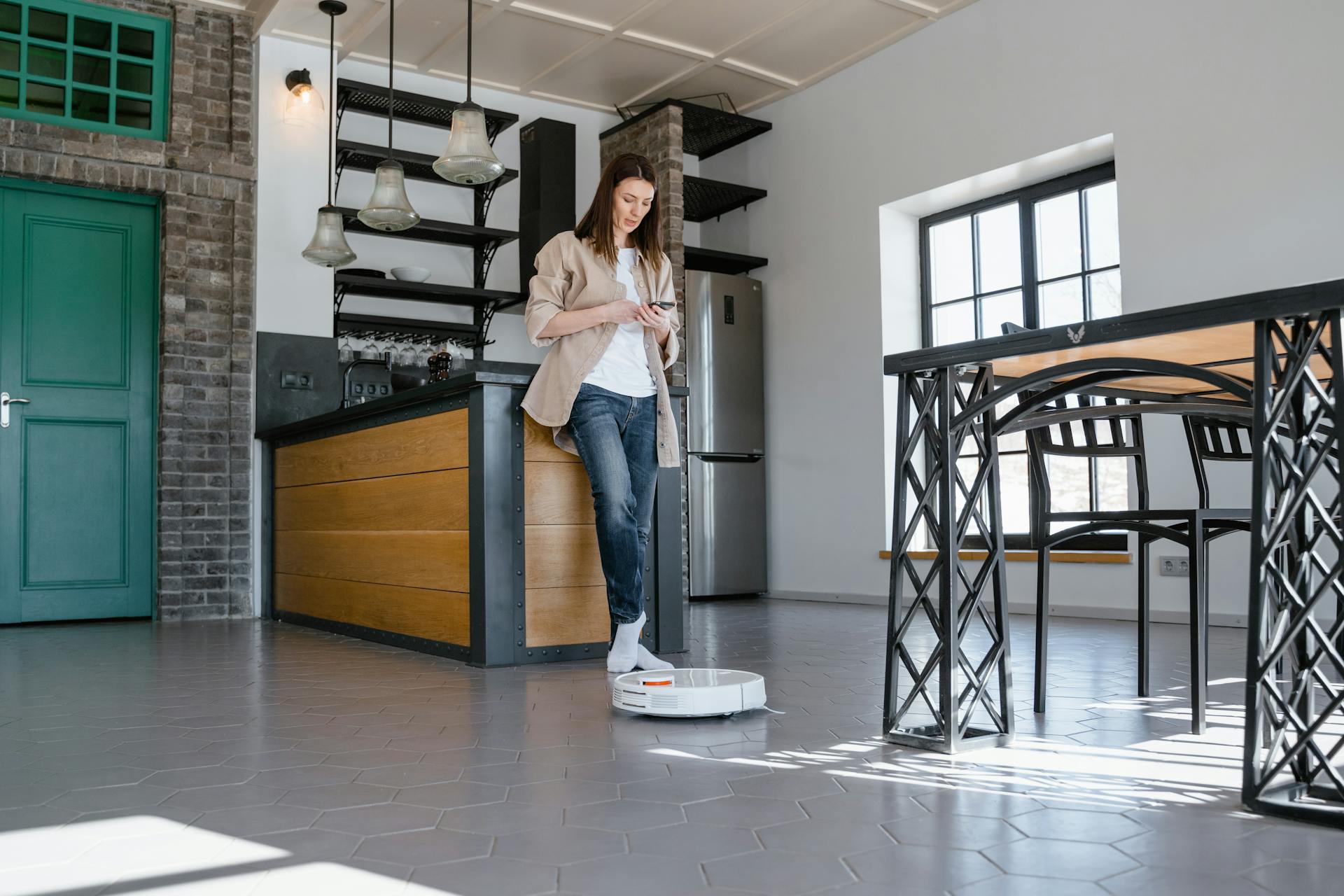 A woman using a robotic vacuum cleaner in a contemporary kitchen setting.