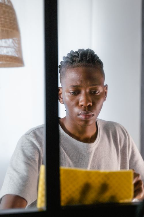 Free A young man uses a yellow cloth to clean a glass window indoors. Stock Photo