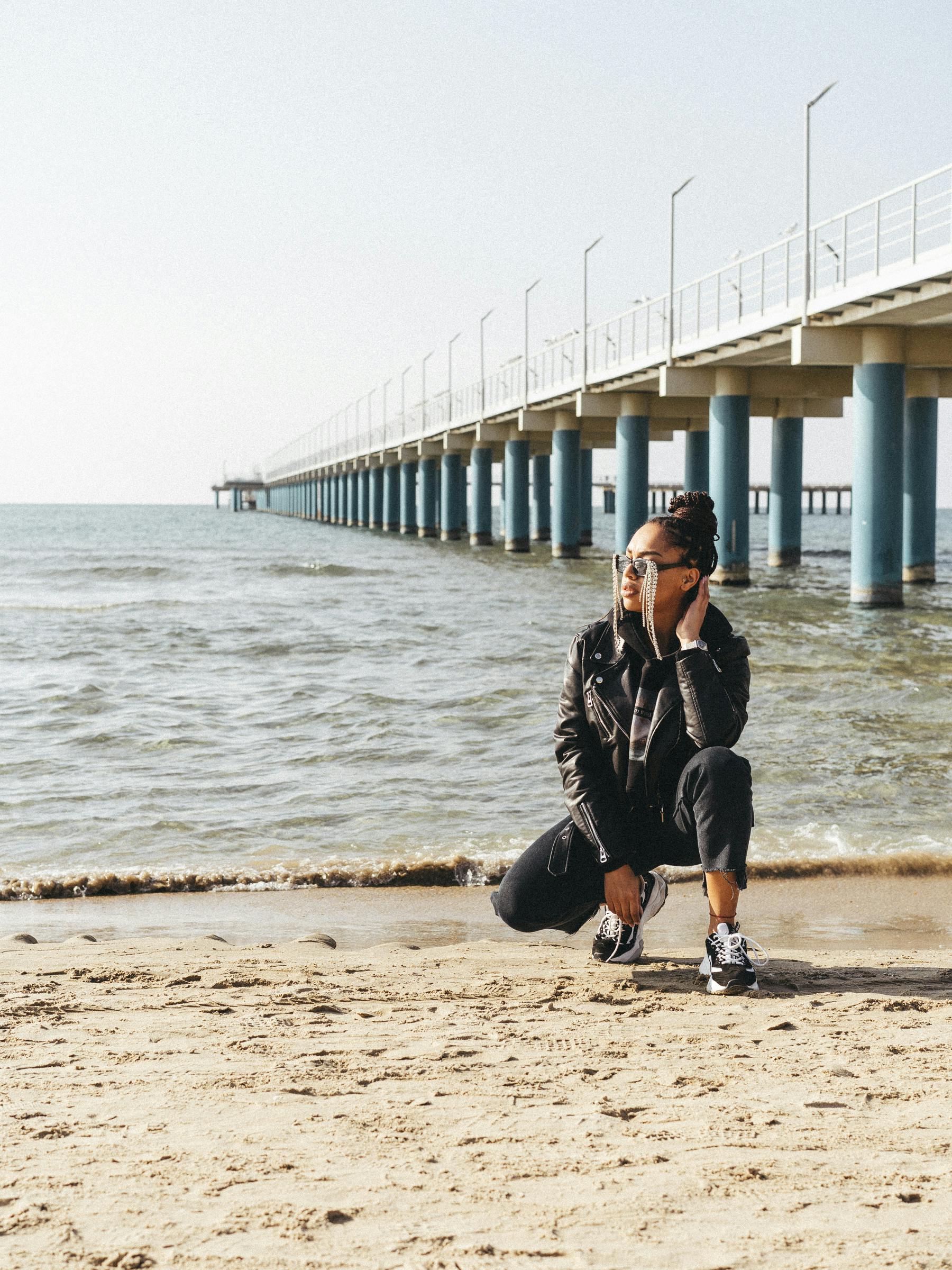 A young woman sits on the sandy beach at Anapa, Russia, near a prominent pier.