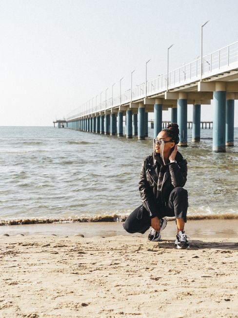 A young woman sits on the sandy beach at Anapa, Russia, near a prominent pier.