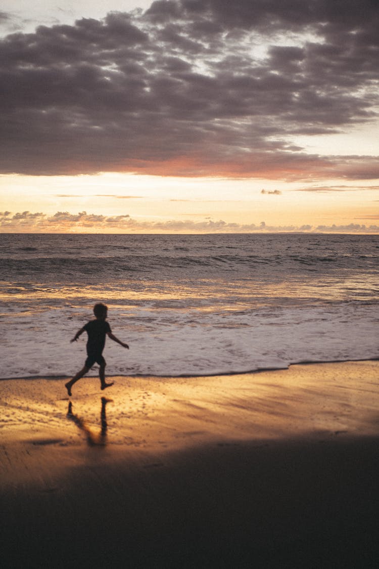 Silhouette Of A Child Running On Seashore During Sunset