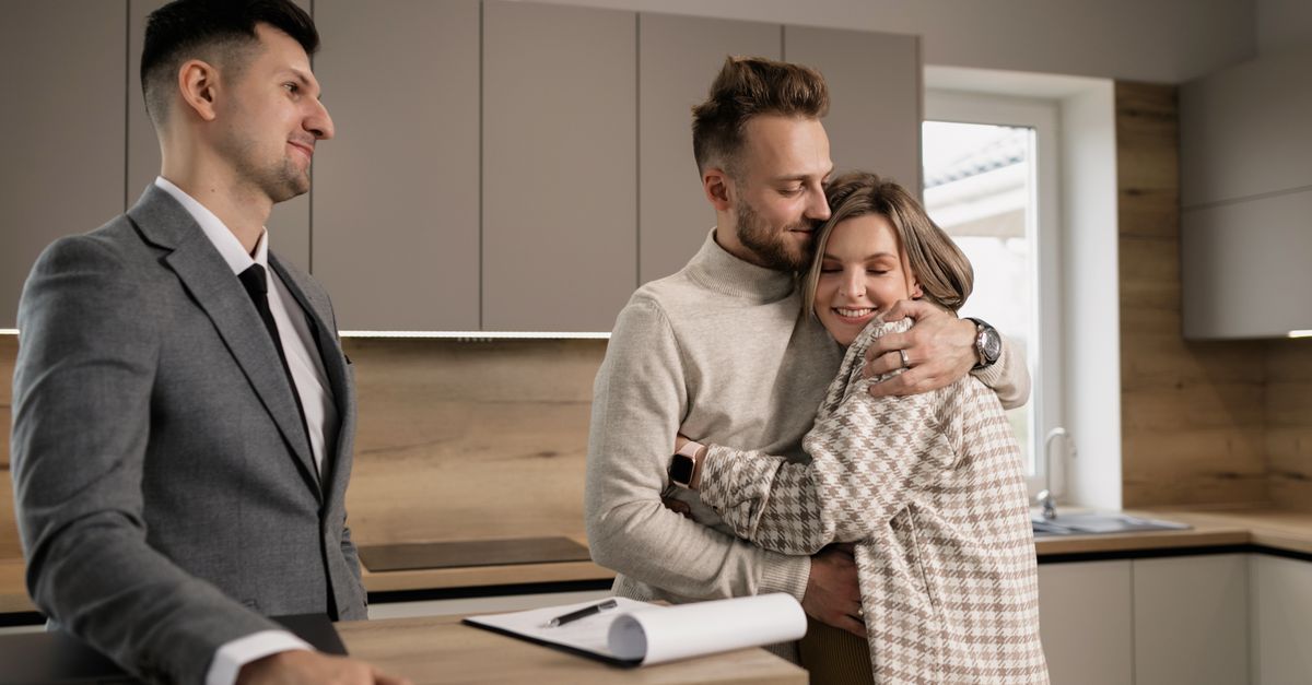 Happy couple embracing in their new home with a real estate agent present.