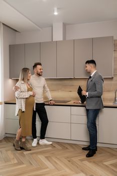 Pregnant couple joyfully discussing their future home purchase with a real estate agent in a modern kitchen.