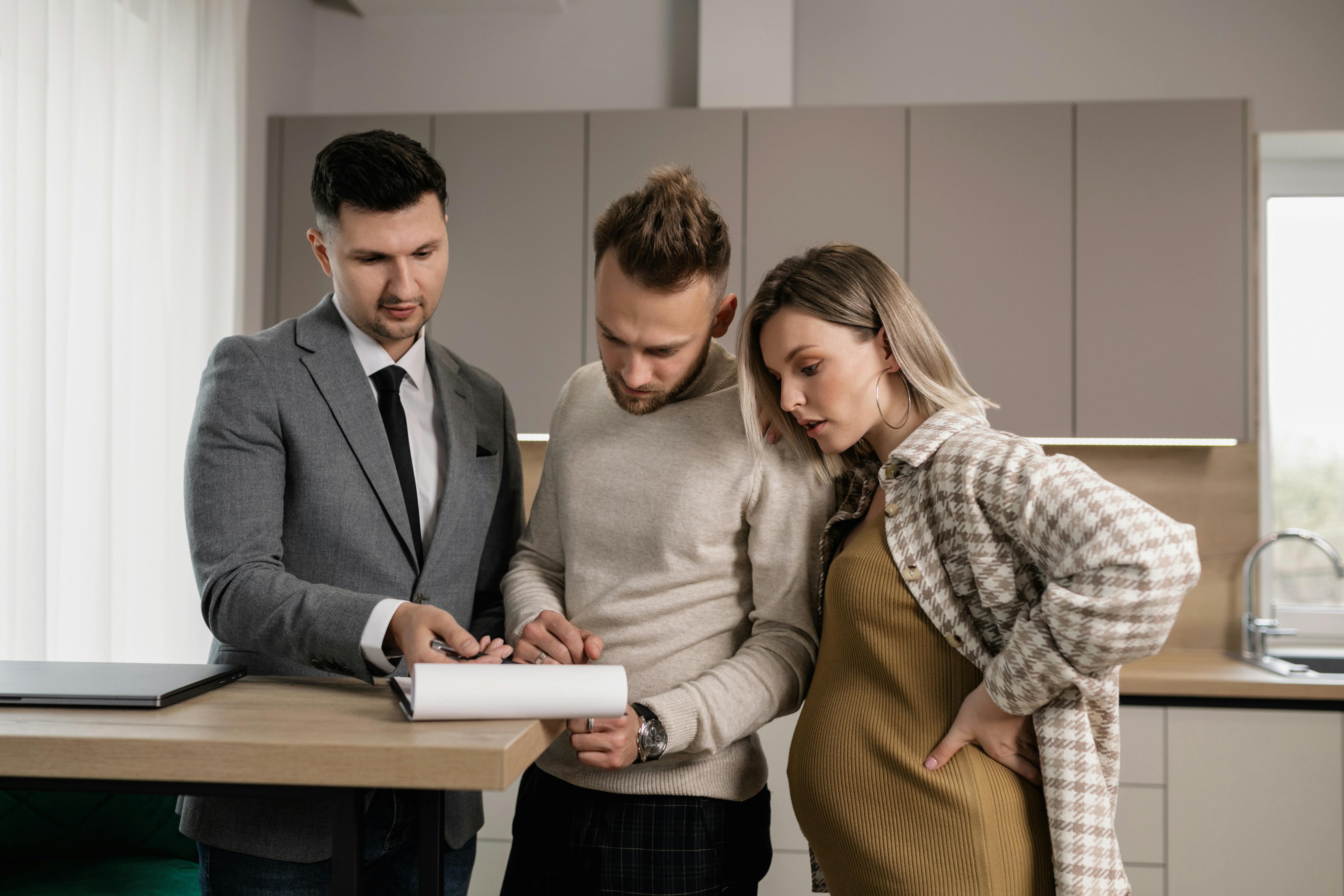 man in gray jacket showing documents to a man and pregnant woman