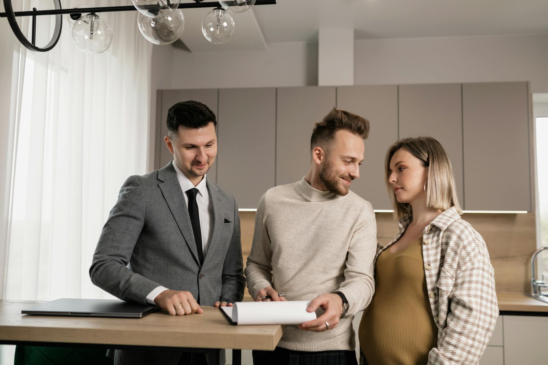 A young couple discusses a real estate contract with a realtor in a stylish modern kitchen.