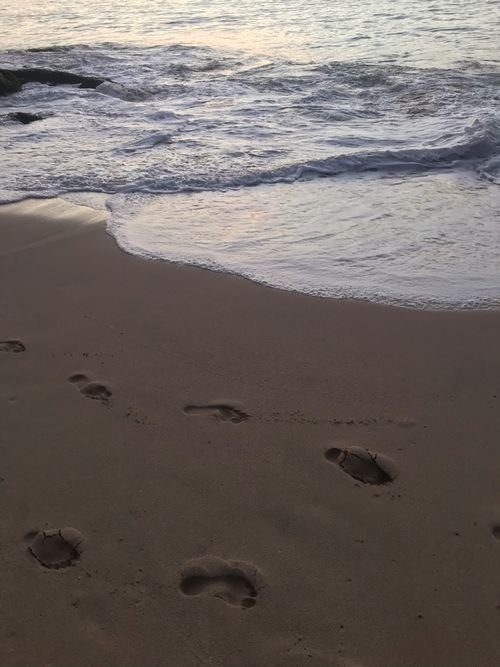 Free Footprints leading to the sea at dusk, capturing the soothing beach waves. Stock Photo