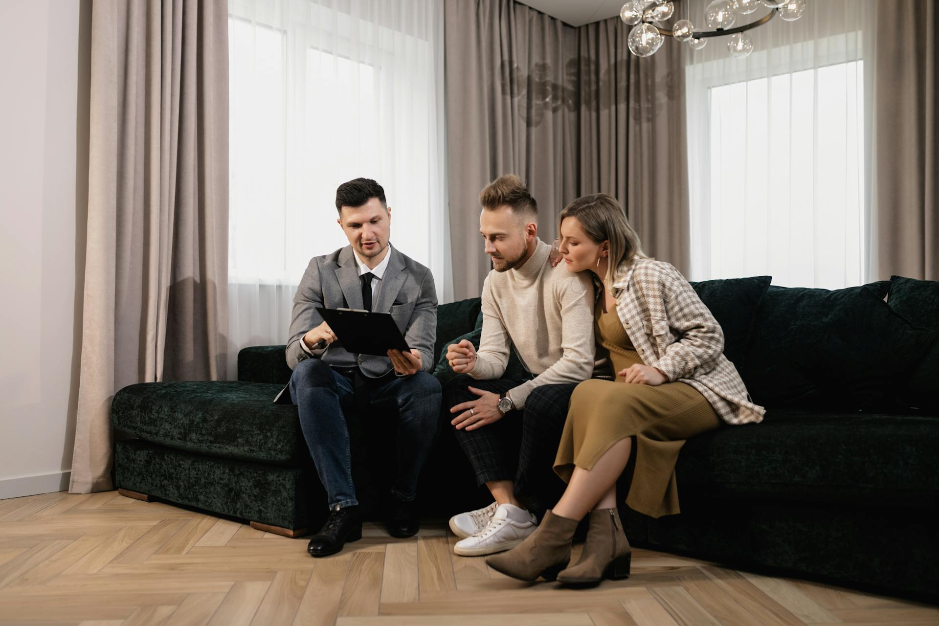 A real estate agent shows a property listing to a couple in a modern living room.