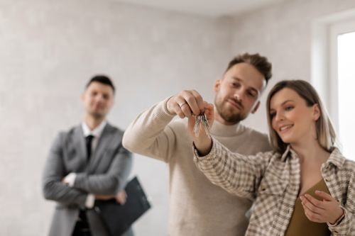 Free A joyful couple holding keys to their new home with a realtor in the background. Stock Photo