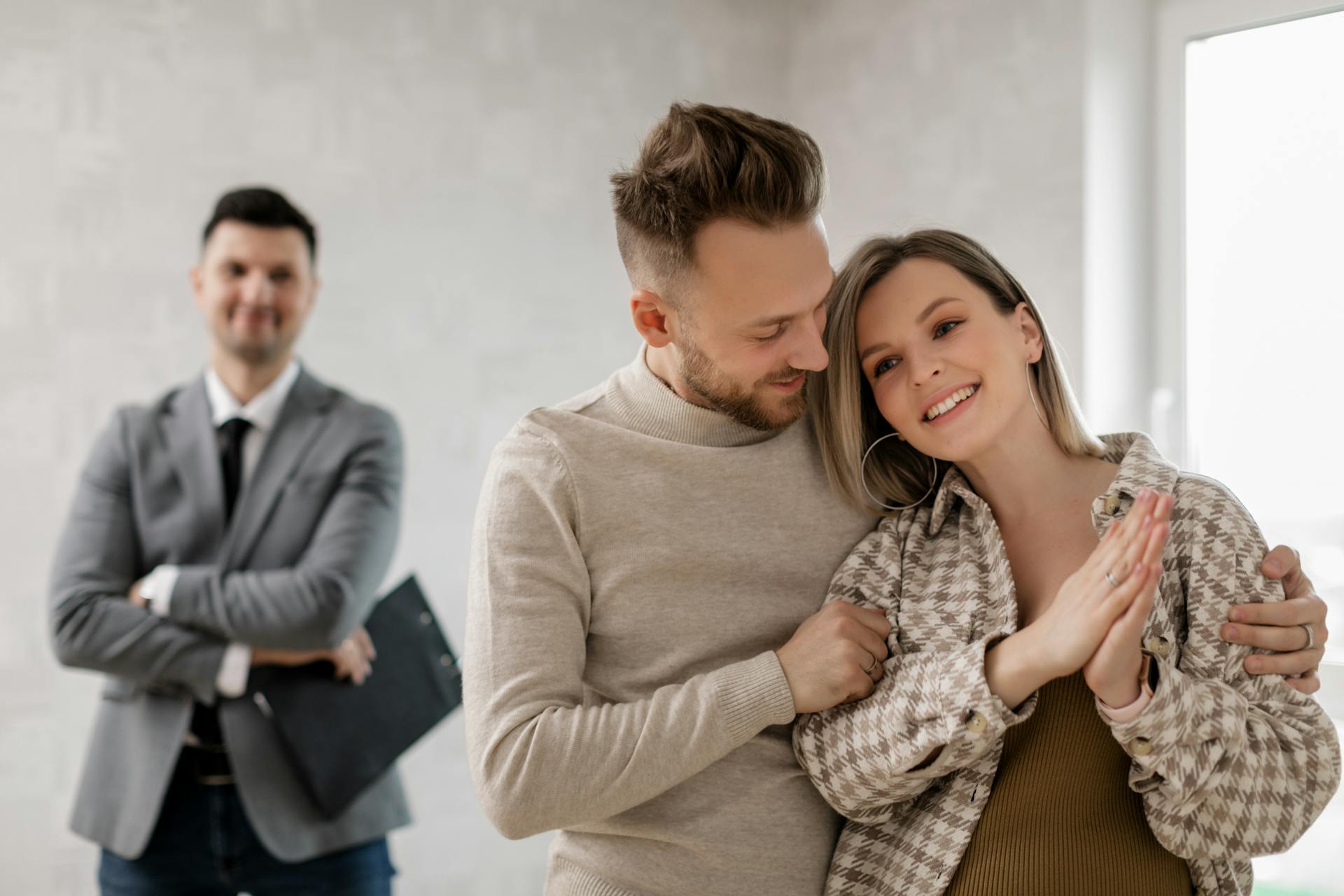 Smiling couple with real estate agent celebrating new home purchase indoors.