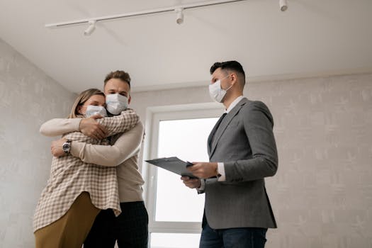 A happy couple in masks hugs in their new home, guided by a realtor.