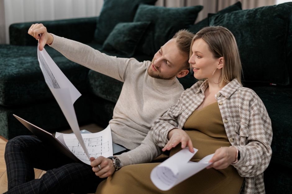 Una pareja sentada en un sofá revisando planos arquitectónicos, simbolizando la compra o renovación de una casa.