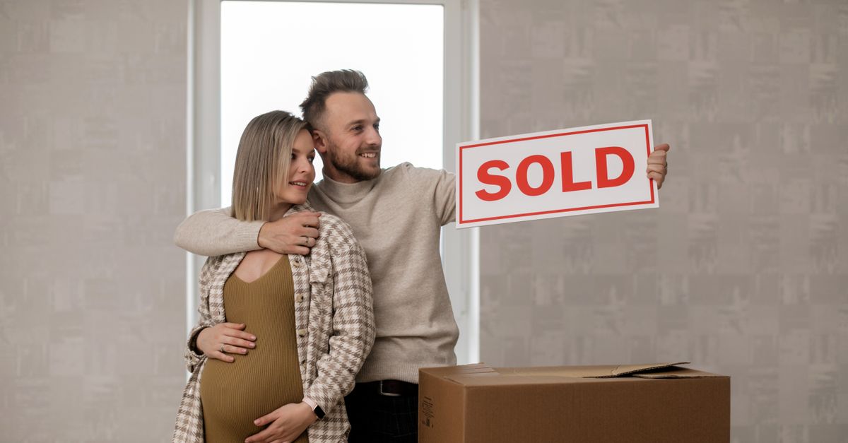 Couple celebrating their new home purchase with a sold sign, symbolizing real estate success.