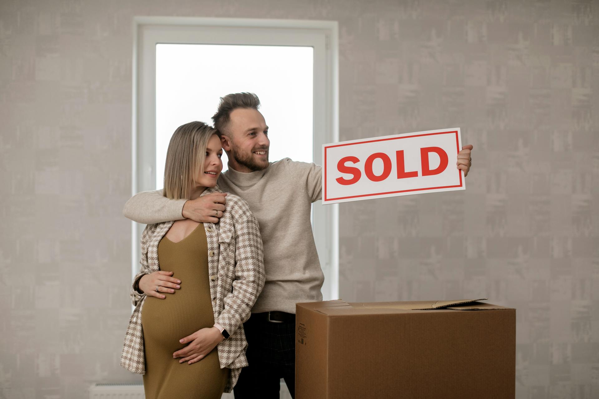 Couple celebrating their new home purchase with a sold sign, symbolizing real estate success.