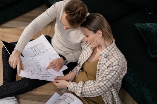 A couple sits on the floor reviewing house blueprints in their living room.
