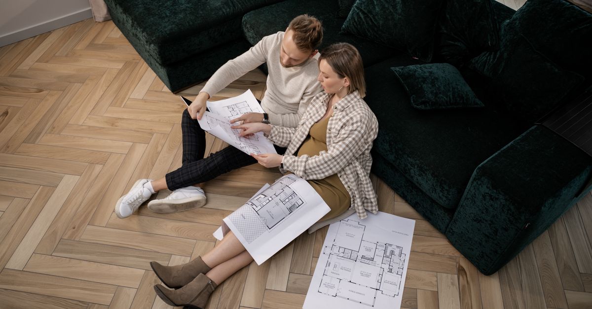 A couple sits on the floor reviewing architectural blueprints, planning their new home.