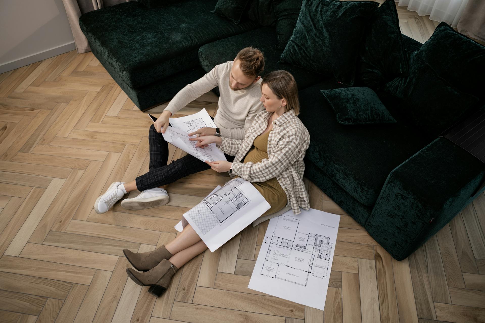 A couple sits on the floor reviewing architectural blueprints, planning their new home.