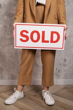 Close-up of real estate agent with sold sign in brown suit indoors.