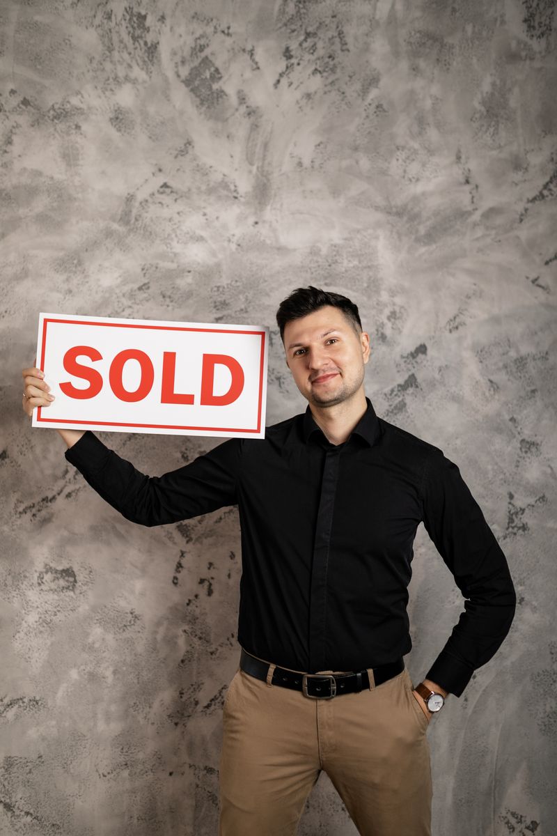 Smiling realtor holding a 'Sold' sign, symbolizing success in real estate transactions.