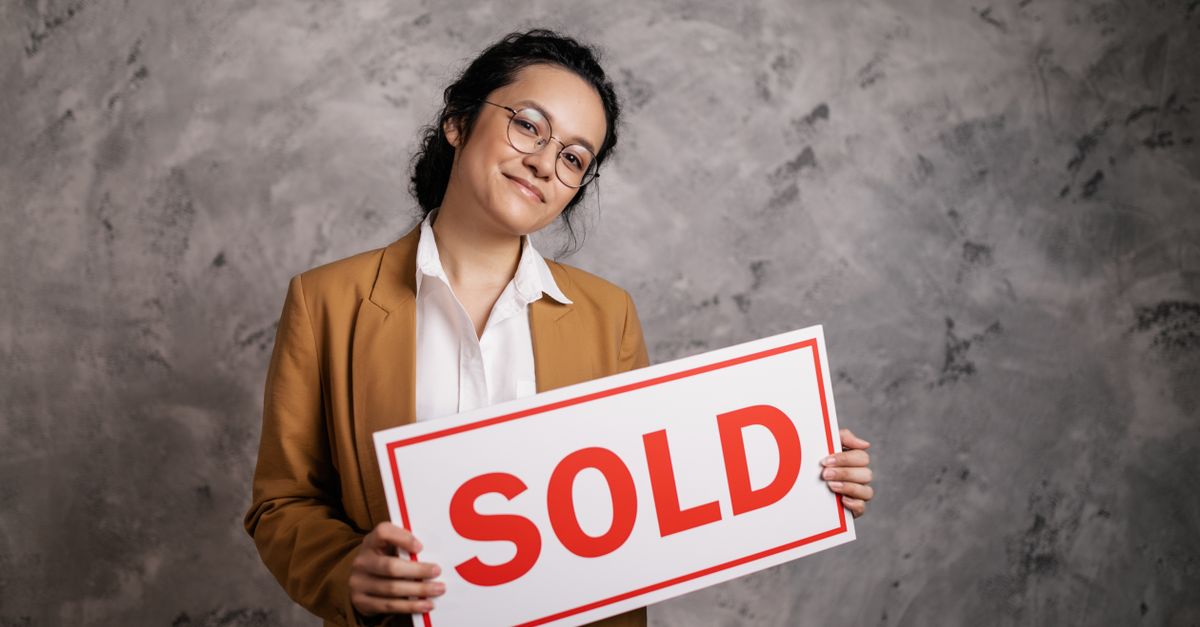 Confident real estate agent holding a 'Sold' sign indoors, symbolizing successful property sale.
