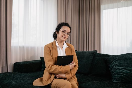Confident woman in business attire sits on a sofa, exuding professionalism.