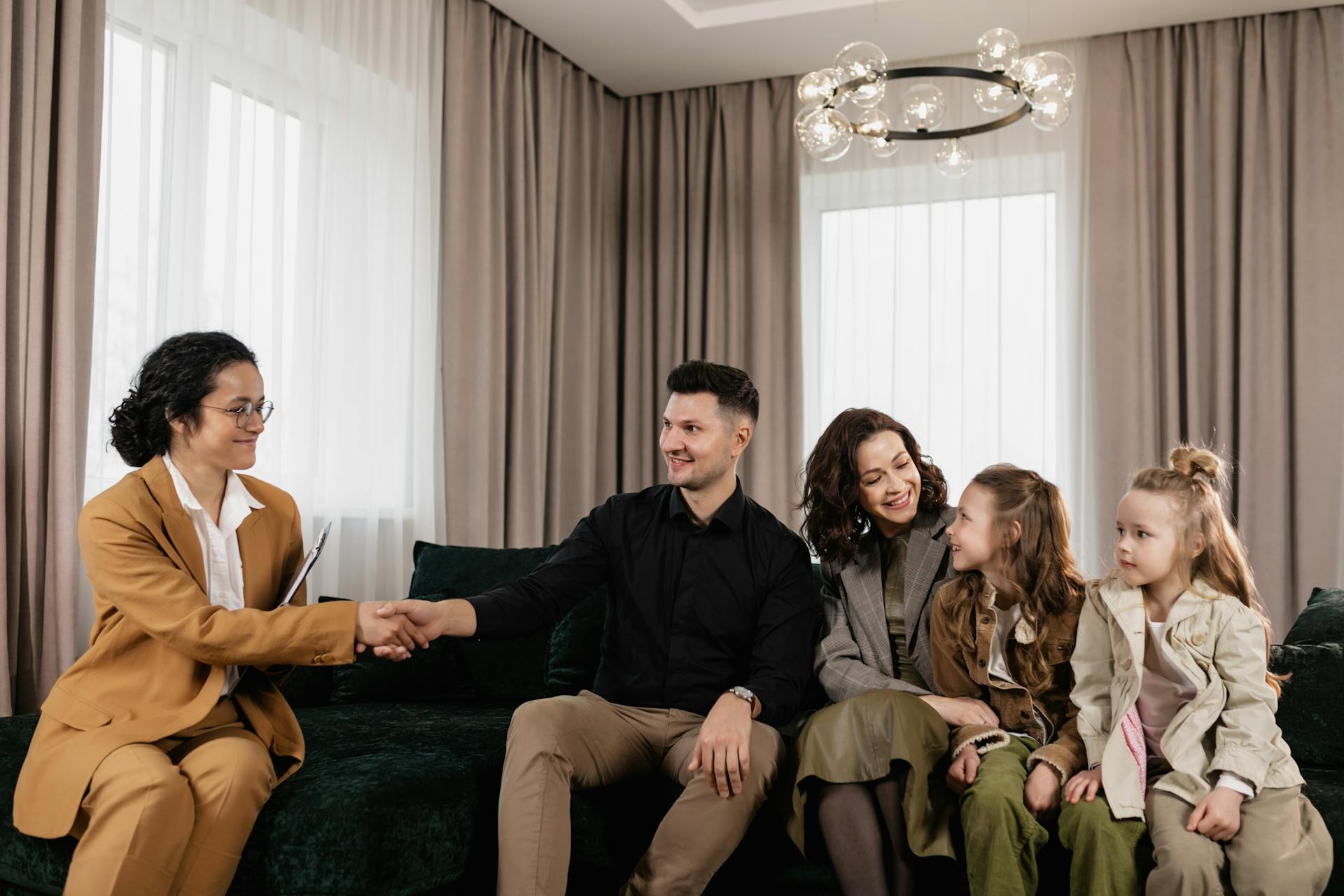 Family sitting on couch having a meeting with a real estate agent indoors.