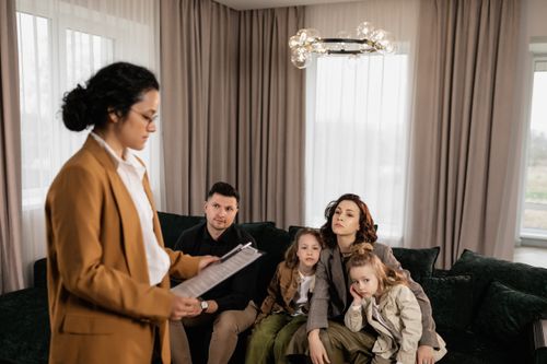 Free Realtor discusses documents with family sitting on sofa in modern living room. Stock Photo