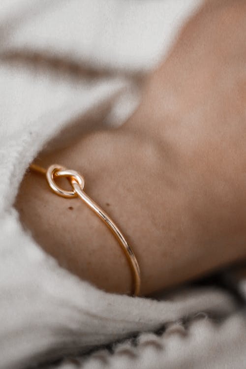 From above of closeup of crop anonymous female with decorative knot shaped golden bracelet