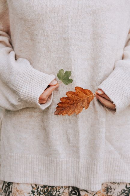 Crop anonymous female wearing warm soft sweater standing with fallen dry leaves in nature