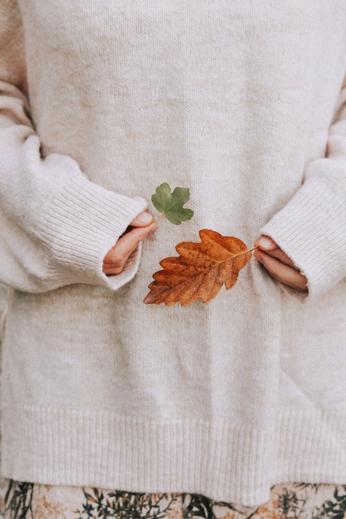 Crop anonymous female wearing warm soft sweater standing with fallen dry leaves in nature