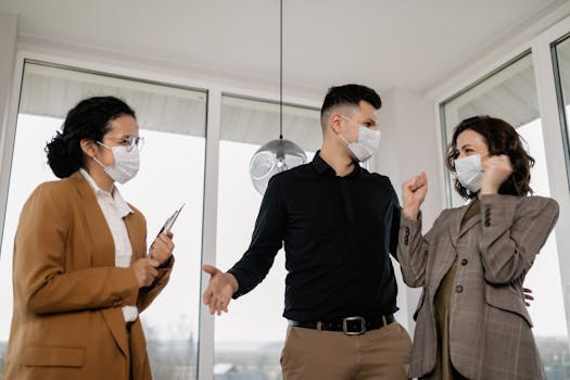 Three adults with face masks discussing real estate indoors joyfully.