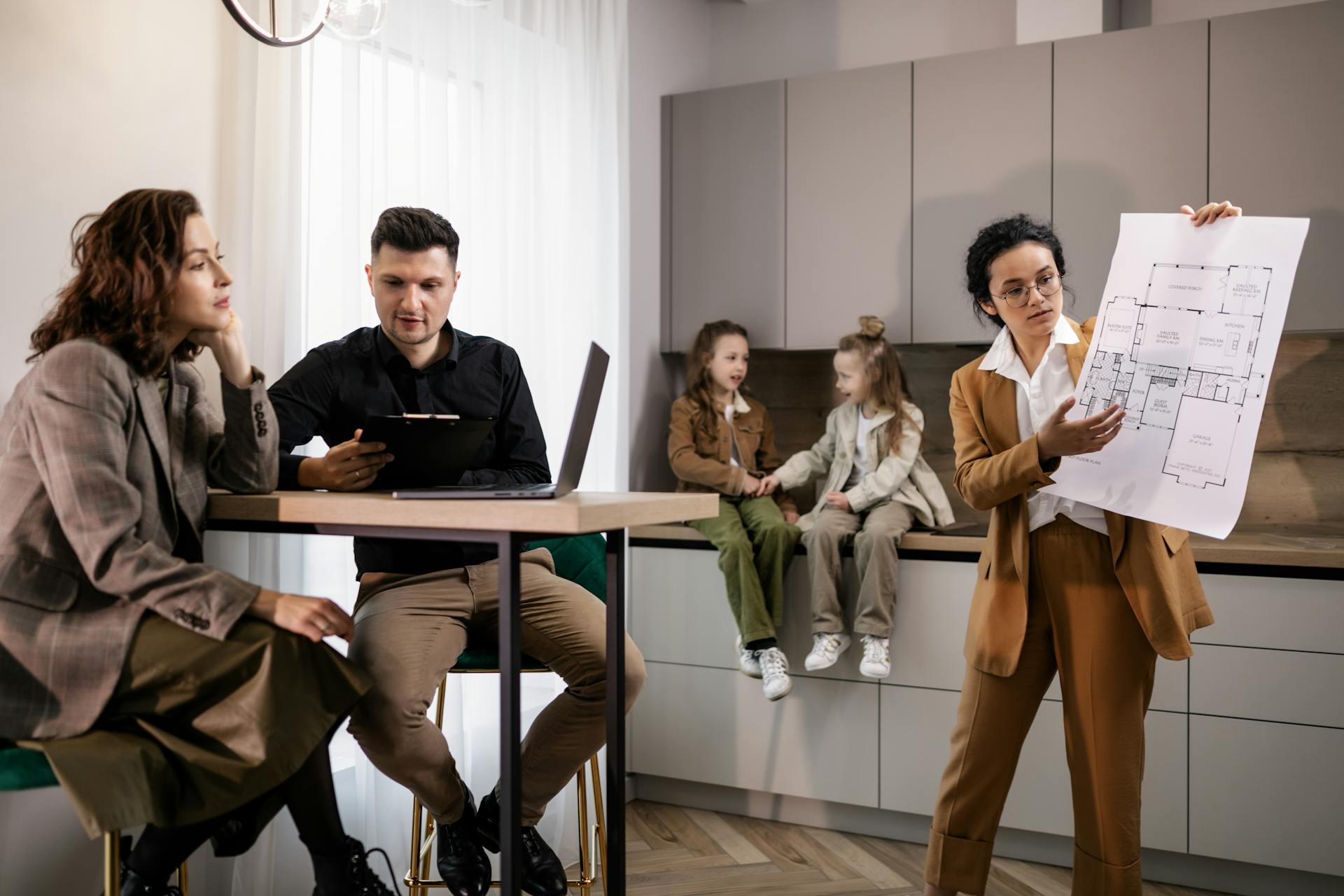 Real estate agent presenting house plans to clients in a modern kitchen setting.