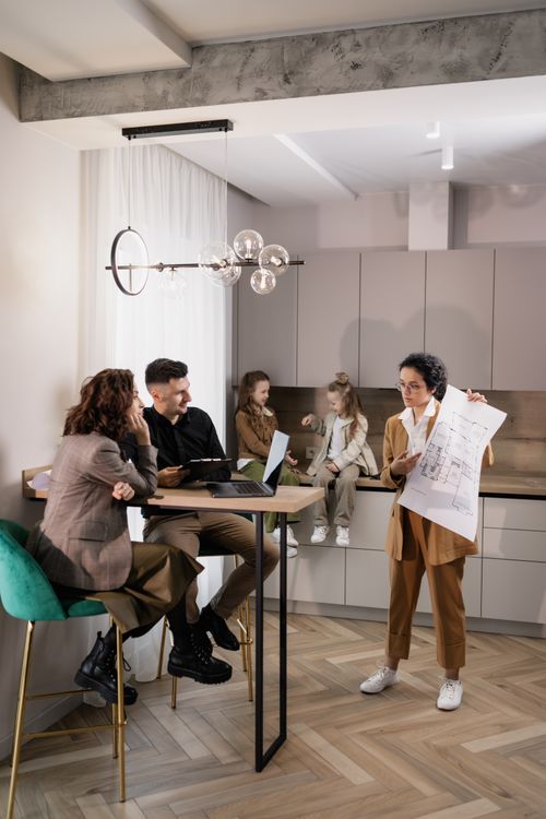 Free Real estate agent presents house plans to a family in a modern kitchen setting, fostering discussion and planning. Stock Photo