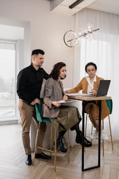 Three young professionals collaborating at a high table, focused on a laptop.