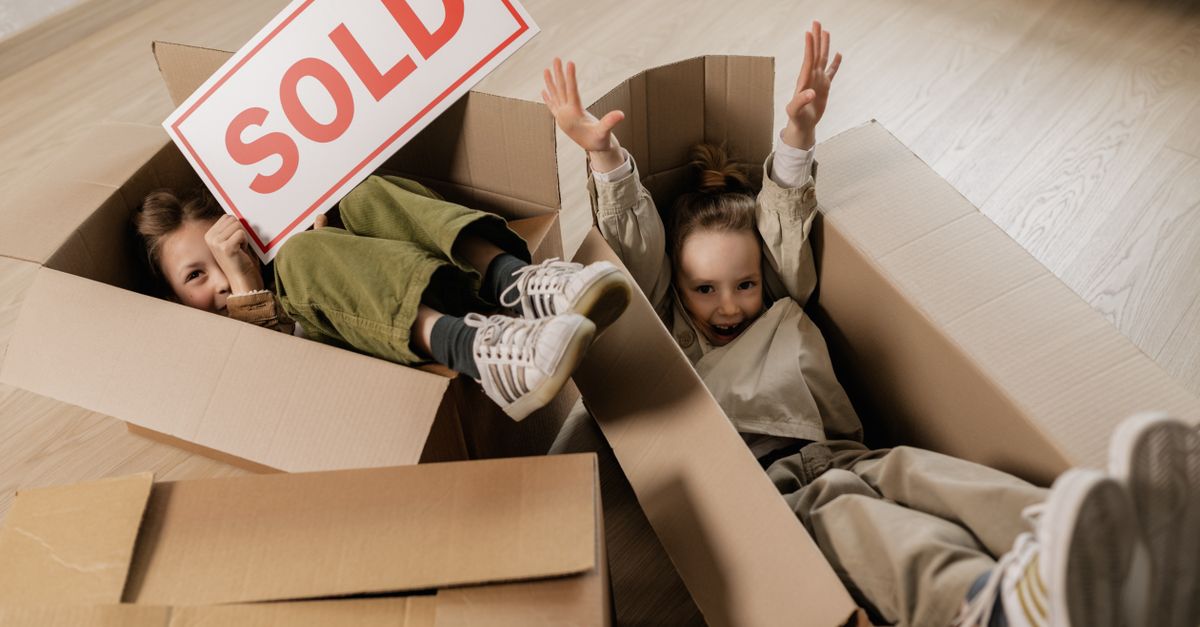 Two happy children playing with cardboard boxes indoors, celebrating moving to a new home.