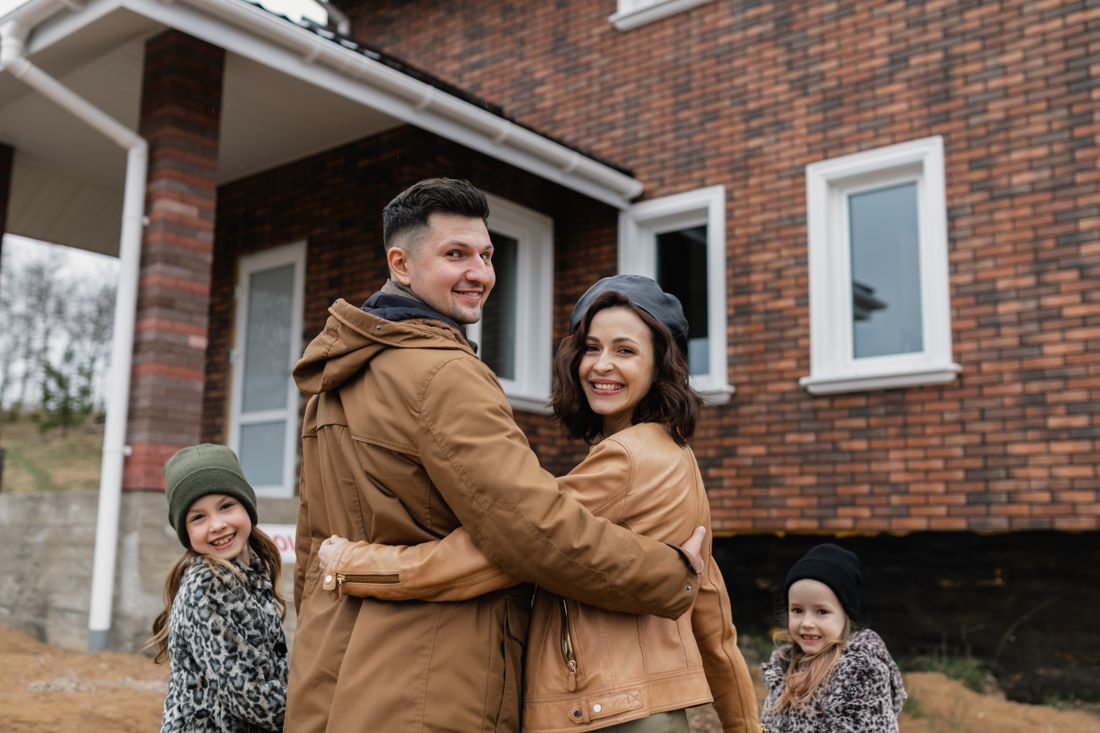 Family of four smiling in front of their home