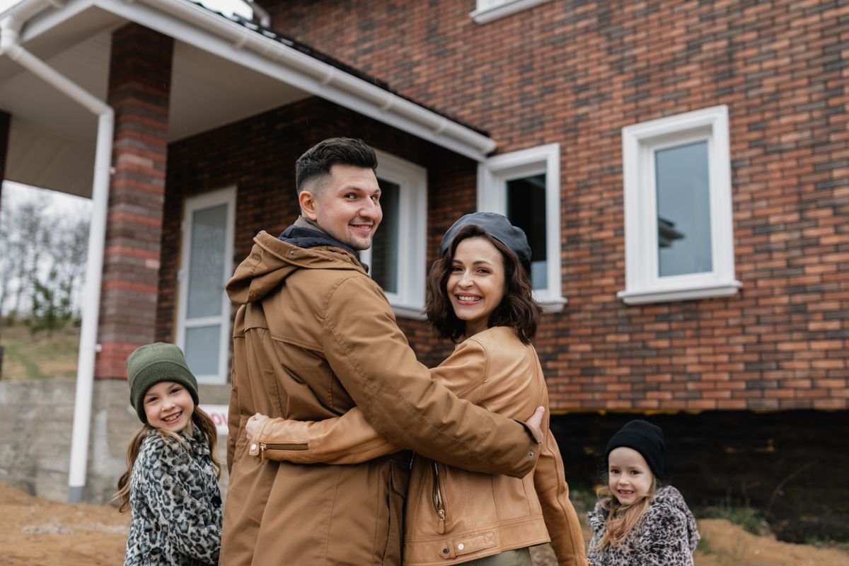 A family of four standing together in front of their new brick home