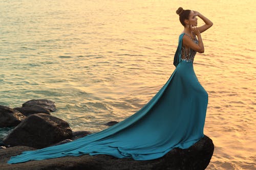 Woman in Blue Dress Standing on Rock Near Body of Water