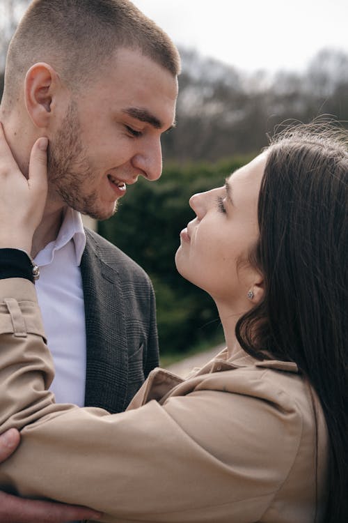 Crop young woman stroking neck of bearded male partner while looking at each other in daylight