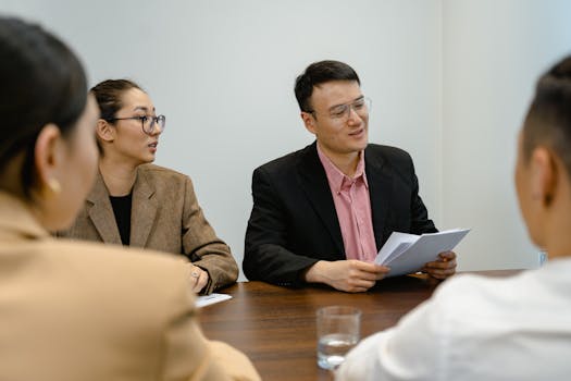 A group of four adults having a business meeting around a table, discussing documents in a modern office setting.