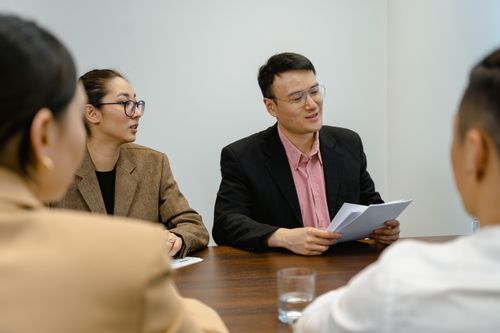 Free A group of four adults having a business meeting around a table, discussing documents in a modern office setting. Stock Photo
