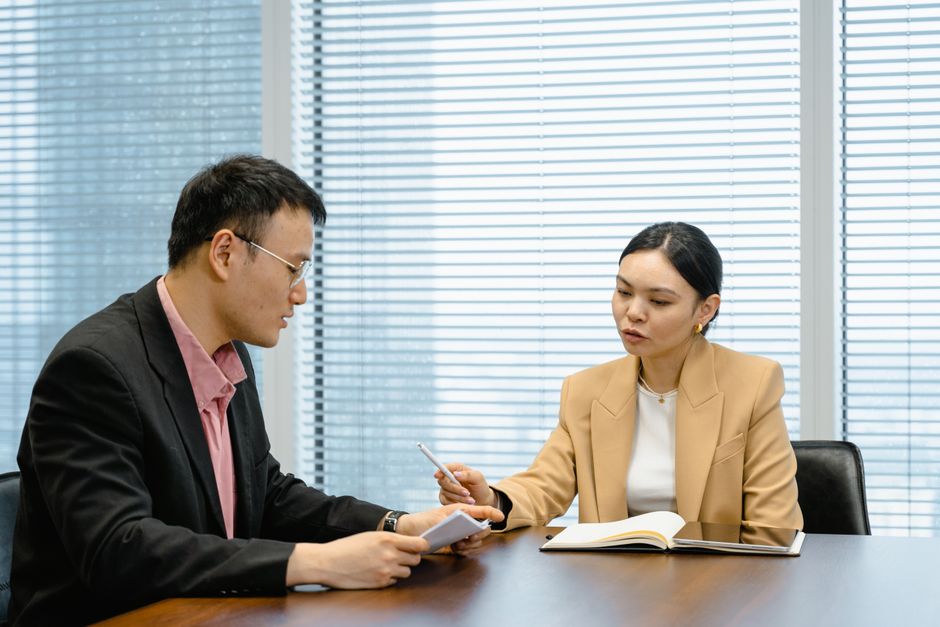 Two professionals in a negotiation meeting in a modern office, one listening to the other