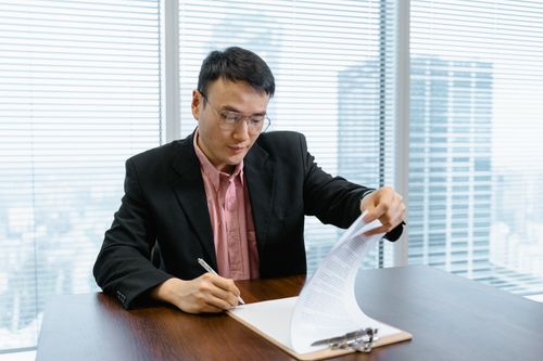 Free Asian businessman in formal wear signs paperwork at office desk. Stock Photo