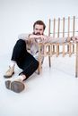Cool bearded male in gumshoes and trousers leaning on chair while looking at camera on light background