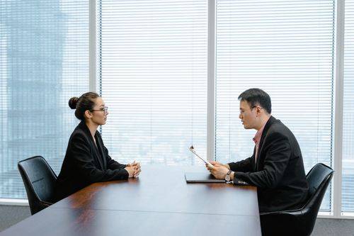 Free Two professionals in a business meeting in a modern office, facing each other across a table. Stock Photo