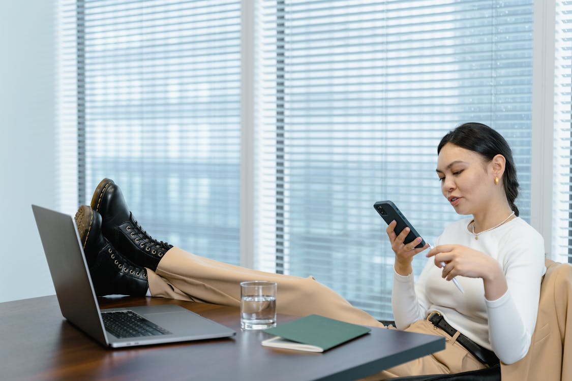 
A Woman Using Her Smartphone in the Office with Her Feet on the Table